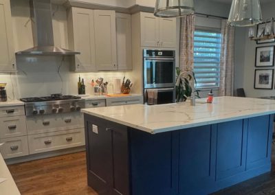 Modern kitchen with white cabinets, blue island, marble countertop, and stainless steel appliances.
